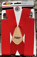 Red suspenders from Kuny's displayed attached to a backing card, showing leather patch with brand logo and metal clips at ends.