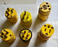 Top-down image showing six yellow Leviton PVC electrical plugs and connectors laid out on a white surface, demonstrating different types and pin configurations.