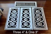 Three decorative metal floor registers with intricate cut-out patterns and one smaller decorative register, all silver/metallic finish.
