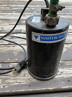Photo of black cylindrical Mastercraft submersible utility pump showing power cord and hose fitting on top.