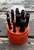 Nine metal punches of varying sizes with silver-colored tips held in an orange plastic cylindrical container.