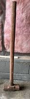 Single photo of a sledgehammer standing vertically against a wall with pink insulation and concrete blocks visible in the background.