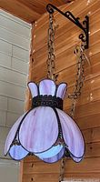 Full view of the hanging purple stained glass light fixture suspended from black metal chain and bracket mounted on a wooden wall.