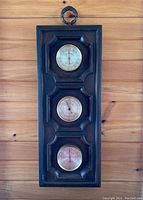 Full vertical view of vintage weather station mounted on wood wall, showing three dials in dark carved wooden frame.