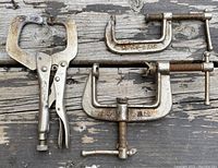 Photo showing one Vise-Grip locking clamp and two metal C-Clamps placed on wood surface.