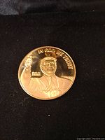 Front side of gold-tone coin showing portrait of Donald Trump, 'IN GOD WE TRUST,' signature, and Made in America text.