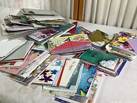 Photo showing piles of unopened greeting cards and envelopes arranged in groups on a table. Cards have a variety of colors and artistic floral and scenic motifs.