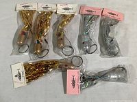 Seven fishing lures in original packaging laid out, showing a mix of gold and silver skirted lures with weighted heads and single hooks.