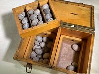 Wooden box open with compartments containing oval lead fishing weights distributed in main sections and lift-out trays.