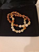 Two handmade bracelets featuring Rudraksha beads combined with natural stone beads and gold-tone charms inside a black display box.