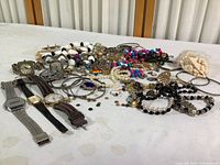 Wide-angle photo showing entire lot spread on table including watches, bracelets, necklaces, earrings, charms, and pins.
