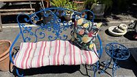 Full view of blue tubular steel bench with striped cushion and floral pillow, and matching side table with ornate scrollwork.