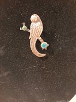 Front view of sterling silver bird brooch with green stones on a black background.