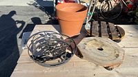 Photo showing all four items: terra-cotta clay pot, two black ornamental metal plant rollers, and one wooden plant dolly roller.