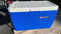 Front view showing the blue body, white lid with slight dent, and Coleman logo on the front side