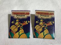 Front view of two matching Disneyland Tomorrowland pins with colorful robotic design and Tomorrowland text on purple background.