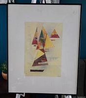 Framed abstract geometric artwork showing colorful triangles and shapes under glass with black frame.