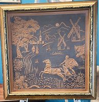 Front of the framed artwork showing embossed rural scene with windmills, horse-drawn chariot, and landscape in a 19x19 gold-tone frame.