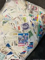 Close-up view of various Canadian postal stamps loose in a plastic bag showing multiple denominations and graphic designs.