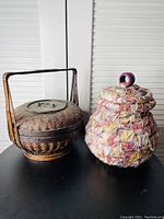 Two baskets side by side, a brown rattan basket with lid and handle and a colorful cloth basket with lid and loop handle