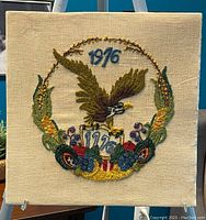 Front view of vintage crewel embroidery textile art showing detailed American eagle with 1776 and 1976 dates and floral corn wreath on cream fabric