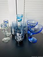 Photo showing a set of 10 drinking glasses including blue swirl goblet, several blue glasses with floral design, and short rimmed glasses.