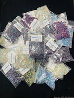 Multiple resealable plastic bags containing various small colored beads arranged on a black surface