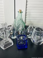 Overview photo showing all glass decor items together including cross, green bottle, teardrop figurines, blue cube, and spherical etched pieces.