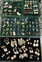 Top-down view showing multiple trays of assorted vintage and modern earrings including studs, dangles, clip-ons, and hoops with various designs and colors.