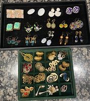 Two trays filled with a variety of vintage and modern earrings of various styles and materials.