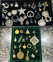 Close view of assorted silver and gold tone pendants and charms arranged on black velvet display, showing various shapes including stars, hearts, crosses, butterflies, and geometric patterns with stones and rhinestones.