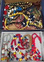 Top view of mixed beaded and wooden necklaces in a box; assorted colors and styles visible.