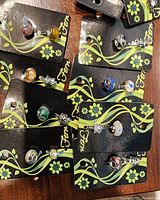Close-up photo showing detailed assortment of Fera glass bead and metal charms on branded cards with floral design.