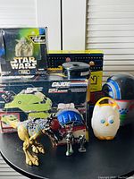 Full view of all toys including boxed Star Wars Yoda, GI Joe Mobile Battle Bunker, K'NEX set, dinosaur figure, metal soldier figurines, owl toy, and robot toy.