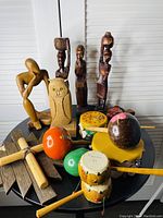 Full view of assorted carved wooden figurines, owl sculpture, wooden percussion instruments, and wooden geometric decor on round surface.