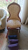 Front view of antique chair showing floral upholstery and wooden carved frame with pillows in front.