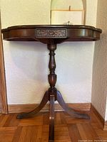 Front view of antique entryway table showing oval wood top and single drawer with carved floral decoration. Central pedestal column and three curved legs visible.