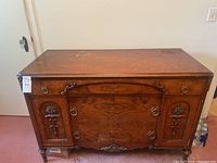 Front view of antique wood dresser showing carved floral door panels, ring pull hardware, and wood grain finish