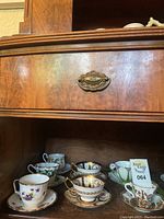 Overview of six assorted tea cups and saucers displayed on wooden shelf