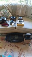 Wide shot showing all items in lot on couch and floor, including binoculars, cameras, radio, earphones, electronic device.