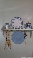Overall view of shelf with blue design ceramics, horse-themed wooden decorations, leather horse collar, and ceramic cups.