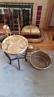 Overview of brass candlesticks, tea pot, wooden stand, brass bowl, and fireplace screen and tools arranged together