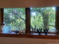 Wide photo showing assortment of candle holders and vases on a window ledge with leafy outdoor background.