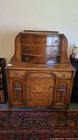 Front view of the antique carved wooden chest of drawers showing the upper section with three curved drawers and lower section with carved floral details on panel sides and three drawers in the middle.
