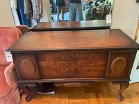 Front view of wooden cedar chest showing decorative rounded panels and cabriole legs with surface wear.