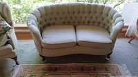 Front view of tufted loveseat showing curved back, seat cushions, wooden feet and overall shape and size.
