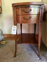 Front view of one wooden side table showing two drawers with metal handles and floral carvings on legs.