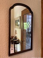 Rectangular wall mirror with an arched top and dark wood frame, mounted on wall.