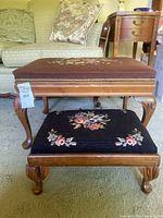 Set of two needlepoint ottomans stacked with upholstered needlepoint floral tops and carved wooden legs, showing overall condition and design.