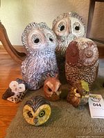 Seven ceramic owl figurines arranged on carpet with some chips visible, tallest approx 14 inches tall.